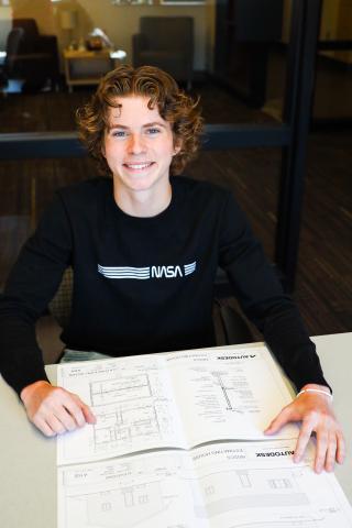 Young man sitting and smiling near building blueprints.