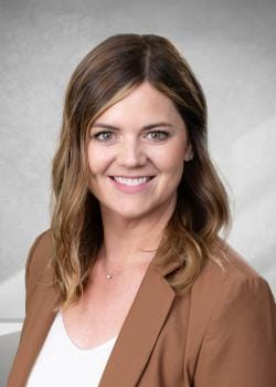Smiling woman with shoulder-length wavy brown hair wearing a brown blazer