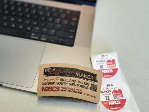 Coffee sleeve and stickers laying next to computer