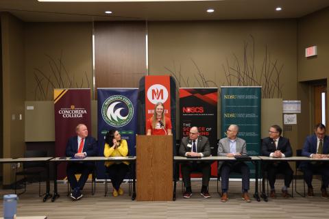 A college student speaks at a podium, flanked by 6 college presidents and administrators