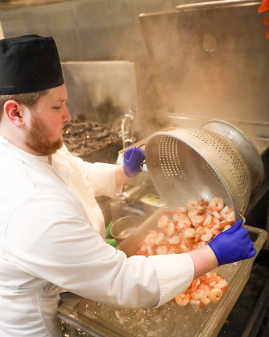 student chef dumping cooked shrimp into bucket of ice to blanch. 