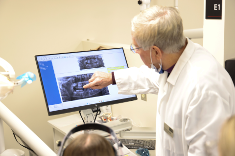 Dentist in white lab coat pointing at xrays on a computer screen.